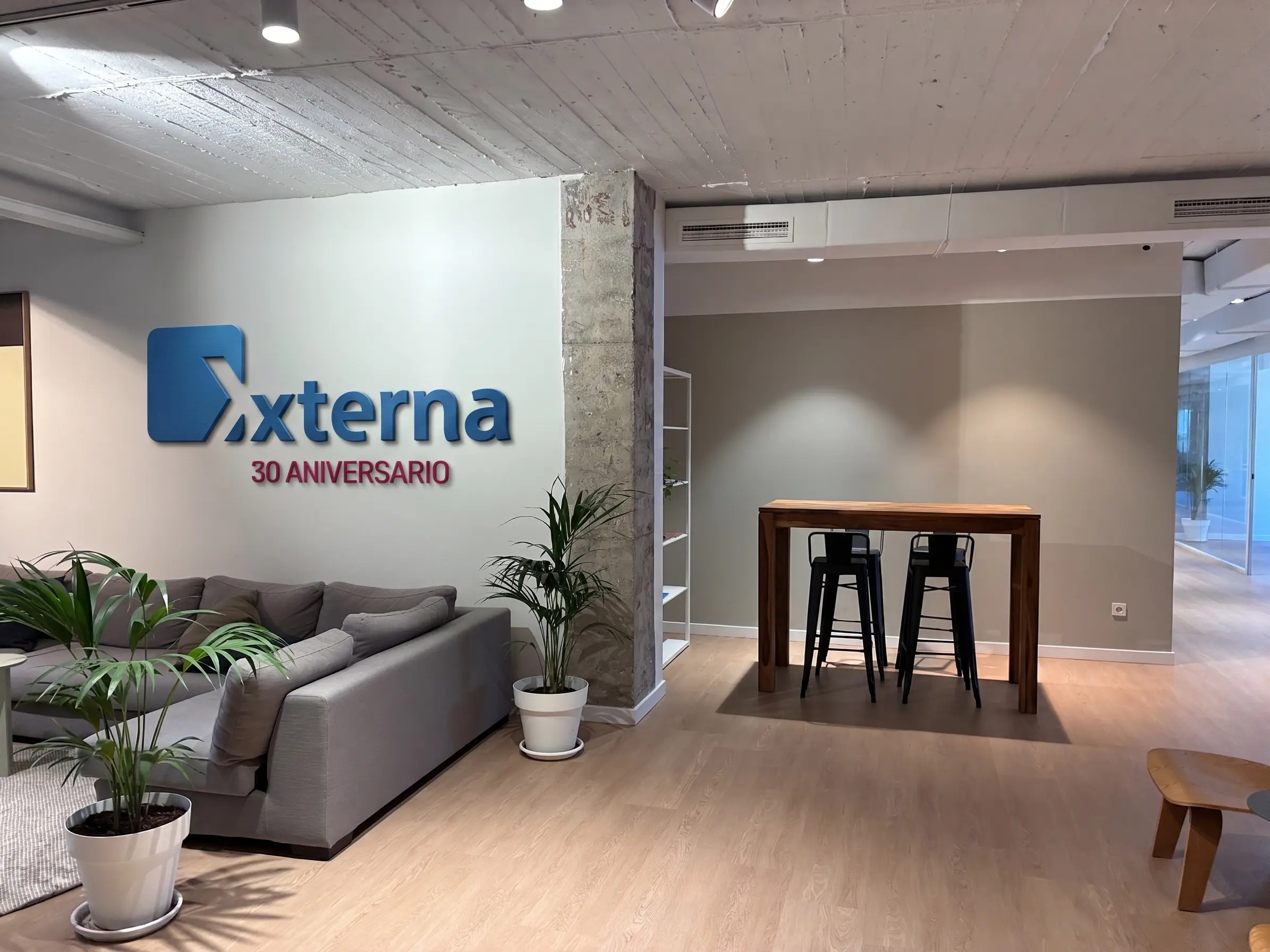 Logotipo de Externa 30 Aniversario en una zona de descanso de oficina con sofás, plantas y una mesa alta